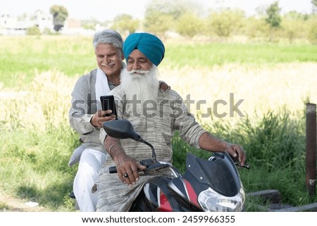 Indian senior  punjabi sikh and non sikh farmers using mobile phone while sitting on motorbike at agriculture filed in village