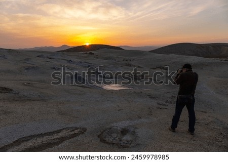 A photographer with a camera takes pictures of mud volcanoes at sunset.