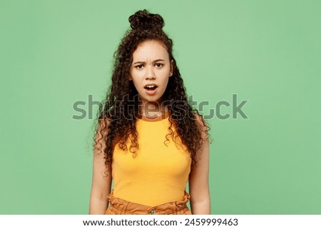 Young sad shocked mad furious woman of African American ethnicity she wear yellow tank shirt top looking camera isolated on plain pastel light green wall background studio portrait. Lifestyle concept Royalty-Free Stock Photo #2459999463