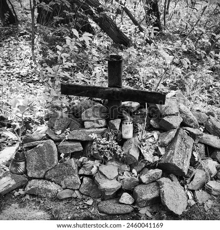 Cross in the ground and stones around it, memorial with a candle, object in nature, magical atmosphere, outdoor, black and white photography