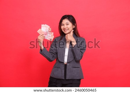 indonesia office woman smiling, holding credit, debit card and money while giving a thumbs up sign to the camera wearing a gray jacket and red skirt. for transaction, business and advertising concepts