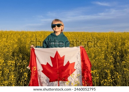 boy wearing hoodie with inscription I am Ukrainian, standing among yellow rapeseed field with Canadian flag . Gratitude to Canada from Ukrainian people for their help and support. Diaspora.