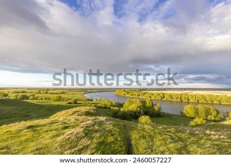  A serene landscape featuring a meandering river with lush greenery on its banks, under a vast blue sky with scattered clouds. The river's curve creates a picturesque scene of natural beauty 