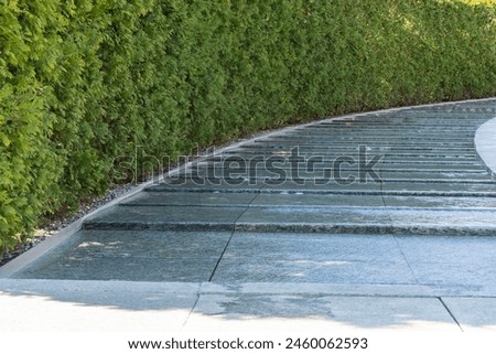 Artificial swift river with granite banks runs around evergreen hedge with rest area. Public landscape 'Galitsky park' for relaxation and walking in sunny spring 2024 Royalty-Free Stock Photo #2460062593