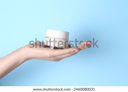Woman holding jar of cream on light blue background, closeup