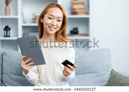 Young Asian Woman With Tablet And Credit Card On Sofa, Smiling At Home, Online Shopping, Modern Technology Usage, Comfortable Living