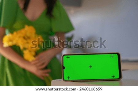 A woman enjoys the aroma of a bouquet of daffodils. Congratulations on the Day of Family Love and Loyalty and Mother's Day. Phone with green screen in the foreground.