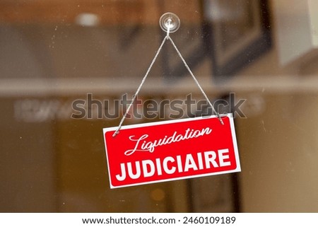 Red sign anging at the glass door of a shop saying in French: "Liquidation judiciaire", meaning in English: "Judicial Liquidation".