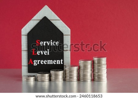 SLA service level agreement symbol. Concept words SLA service level agreement written on a black board. Silver coins arranged in a graph in front. Beautiful red background, grey table. Business concep