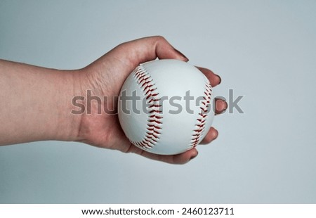 Hand with brown nail polish holding white and red baseball soft ball equipment sphere object photography isolated on horizontal ratio plain white or light gray background.
