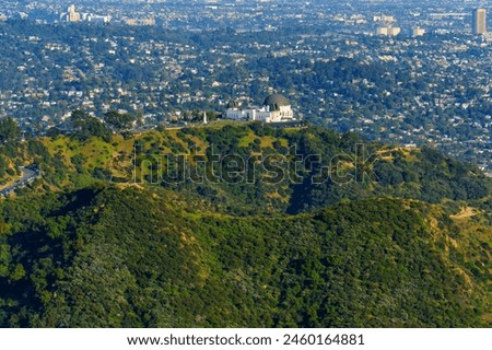 Griffith Observatory as seen from above, perched atop verdant hills against the backdrop of the cityscape on a tranquil April day.