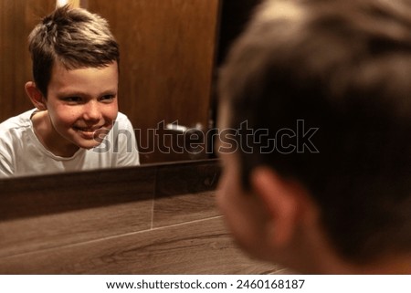 Adorable healthy boy watching at himself in mirror in bathroom in the night at home.
