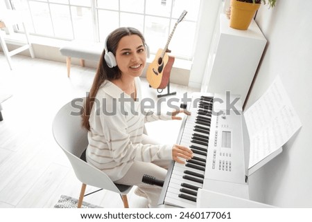 Beautiful young happy woman in headphones listening music and playing synthesizer at home Royalty-Free Stock Photo #2460177061