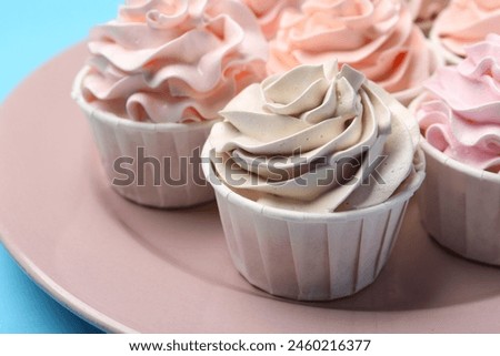 Plate with tasty cupcakes on light blue background, closeup