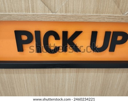Pick Up Sign in A Fast Food Restaurant. Signage Showing Customer The Place To Pick Food Up. Black Text with Orange and Wooden Background. Area To Take Your Food.