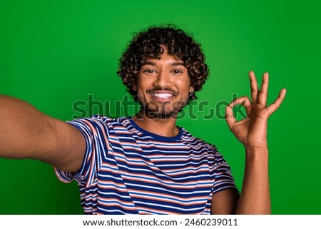 Photo of cheerful positive man wear trendy striped clothes live stream blog okey sign isolated on green color background