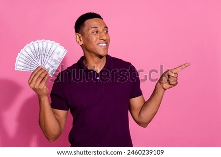 Photo portrait of handsome young guy hold money fan point look empty space wear trendy violet outfit isolated on pink color background