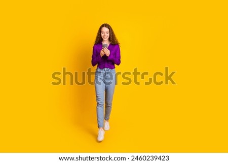 Full length photo of lovely young lady walk hold gadget dressed stylish violet garment isolated on yellow color background