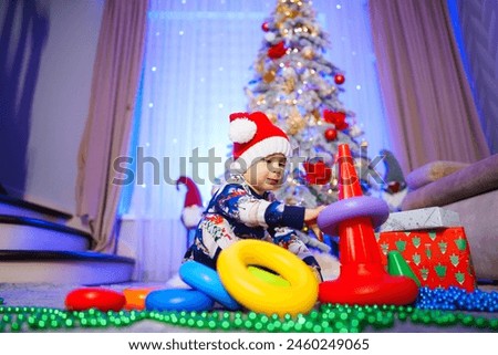 A young child is playing with a set of plastic rings in front of a Christmas tree.