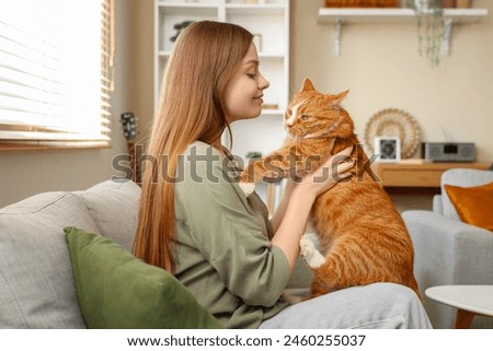 Young woman with cute red cat sitting on sofa at home