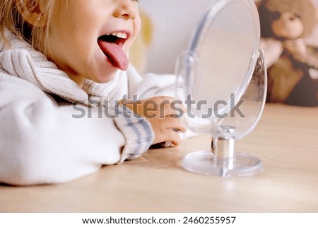 blonde girl of 3 years old girl in front of mirror engaged with speech therapist, gymnastics for tongue, defect, speech disorder with frequent repetition sounds, syllables, spasms muscles apparatus Royalty-Free Stock Photo #2460255957