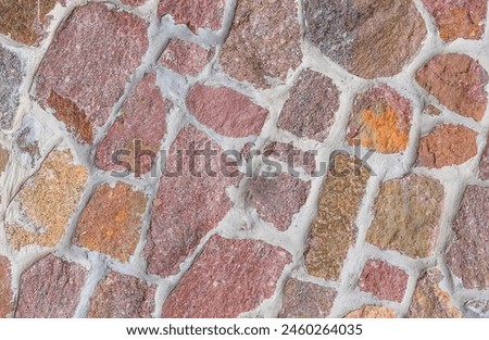 It's close up view of the colorful wall. Its photo of multicolor stonewall. It is photo of multicolored srone wall. its view of red sidewalk. It's view of mosaic stonewall