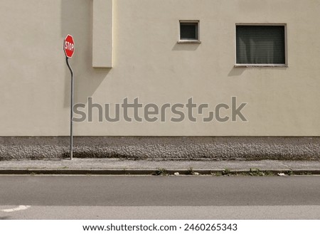 Stop traffic sign on concrete sidewalk. Pale yellow plaster facade with windows on behind,  urban street in front. Background for copy space.