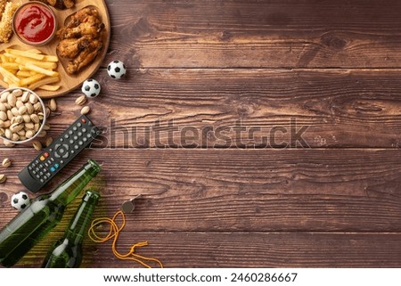 Top view of wooden table with football snacks including beer, fries, chicken wings, and remote, styled with miniature soccer balls