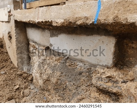 Construction site showing wall underpinning with new and existing concrete. Detailed view of building foundation. Design for educational material, construction training. Royalty-Free Stock Photo #2460291545