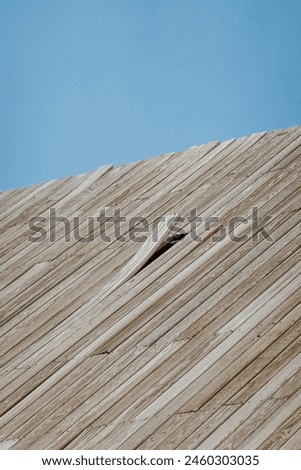 Close-up of a textured wooden surface, angled against a clear blue sky, emphasizing the natural wood grain and linear patterns. Royalty-Free Stock Photo #2460303035