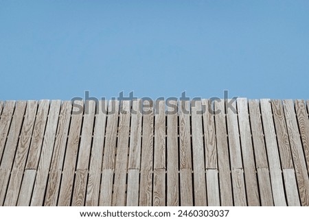 Close up of a textured wooden surface, angled against a clear blue sky, emphasizing the natural wood grain and linear patterns. Royalty-Free Stock Photo #2460303037