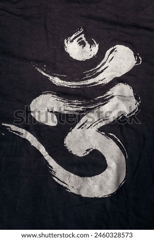 Om word on dark background. Spiritual sign isolated. Sacred Om symbol printed on clothes. Sanskrit magic word. Indian calligraphy on printed fabric. Om mantra. Powerful religious symbol.
