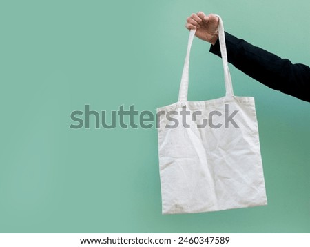 Woman in classic black blazer holding tote canvas blank eco bag on street green minimal wall background. Female consumer hold white textile shopper. template or place for your design, logo or text
