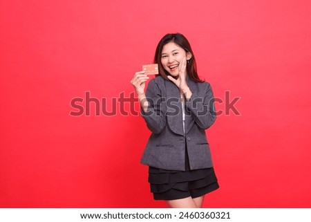 Cheerful indonesia businesswoman expression hand to mouth and holding debit credit card wearing jacket and skirt on red background. for financial, business and advertising concepts
