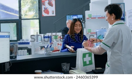 Asian customer at pharmacy counter, showing druggist prescribed heart medicine picture on smartphone, ready to purchase it. Healthcare expert selling client required medicinal product