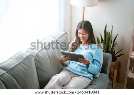 relaxation, enjoying, literature, smiling, happy, lying, living, reading, social, pad. A woman is sitting on a couch and looking at a tablet. She is smiling and she is enjoying her time.