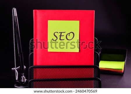 SEO business, SEO concept. Search engine optimization text on a yellow sticker on a red notepad in front of a black background. A place to copy