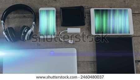 Image of light trails over technological devices with colorful moving shapes on screen on desk. Global technology, abstract background and digital interface concept digitally generated image.