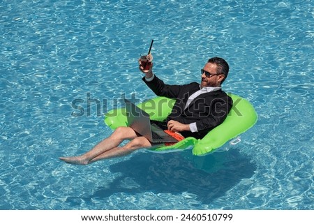 Successful business man floating in suit in pool water. Summer vacations and travel concept. Funny business man drink summer cocktail and using laptop in swimming pool. Summer business concept.