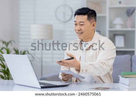 Asian man interacts with a webinar on his laptop at home, expressing happiness and engagement. This image captures the joy of lifelong learning and the convenience of online education.