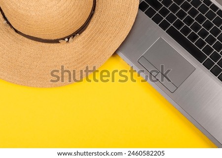 Laptop and straw hat on yellow background. Work at holiday. Concept of travelling on summer vacation. Business trip to the south. Freelancer's job. Working weekend. Visiting card with empty text place