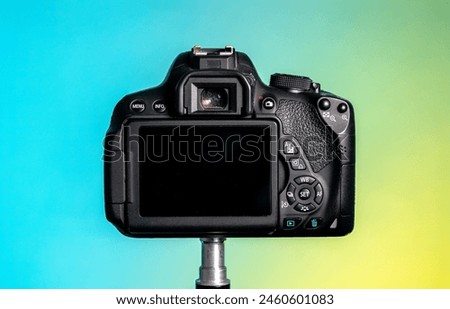Black digital camera photograph from behind, view of buttons, camera screen, viewfinder and grip. Coloured background.