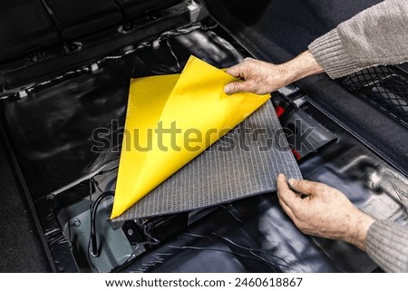 Auto service worker installing soundproofing foam material on car door trim from inside, tuning car sound or installing noise insulation. Process of car sound insulation installation.