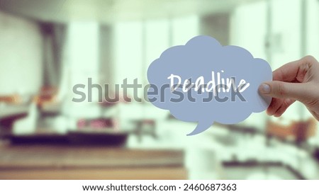 "Deadline" on a white office background. A hand holds this sign in the air.