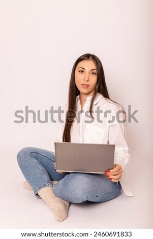 A young woman in a white shirt with a laptop sits on a white background. Follow-up work. High quality photo