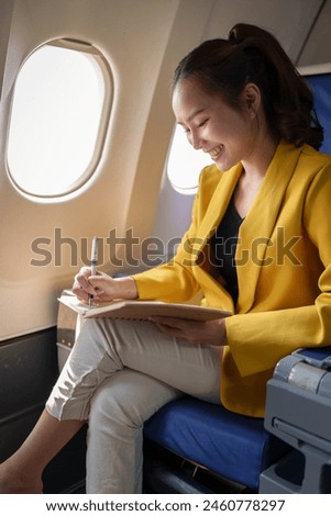 Beautiful successful Asian businesswoman sitting in a plane and working on a notebook. Notes, ideas, business presentation guidelines in first class. Business tourism concept.