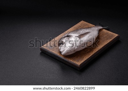 Whole raw dorado fish with lemon, salt, spices and herbs on a dark concrete background
