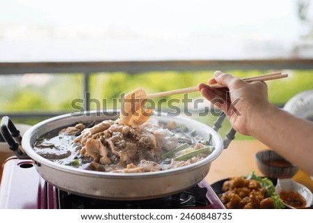 Slice of pork was picking up by the chopstick in the woman's hand above the curved brass pan around with diffused smoke. Royalty-Free Stock Photo #2460848735