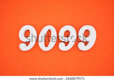 The number 9099 is made from white painted wood placed on a background of orange paper.