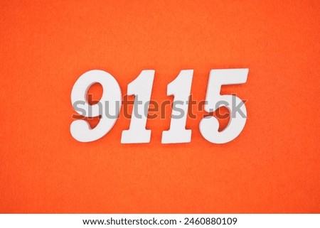 The number 9115 is made from white painted wood placed on a background of orange paper.